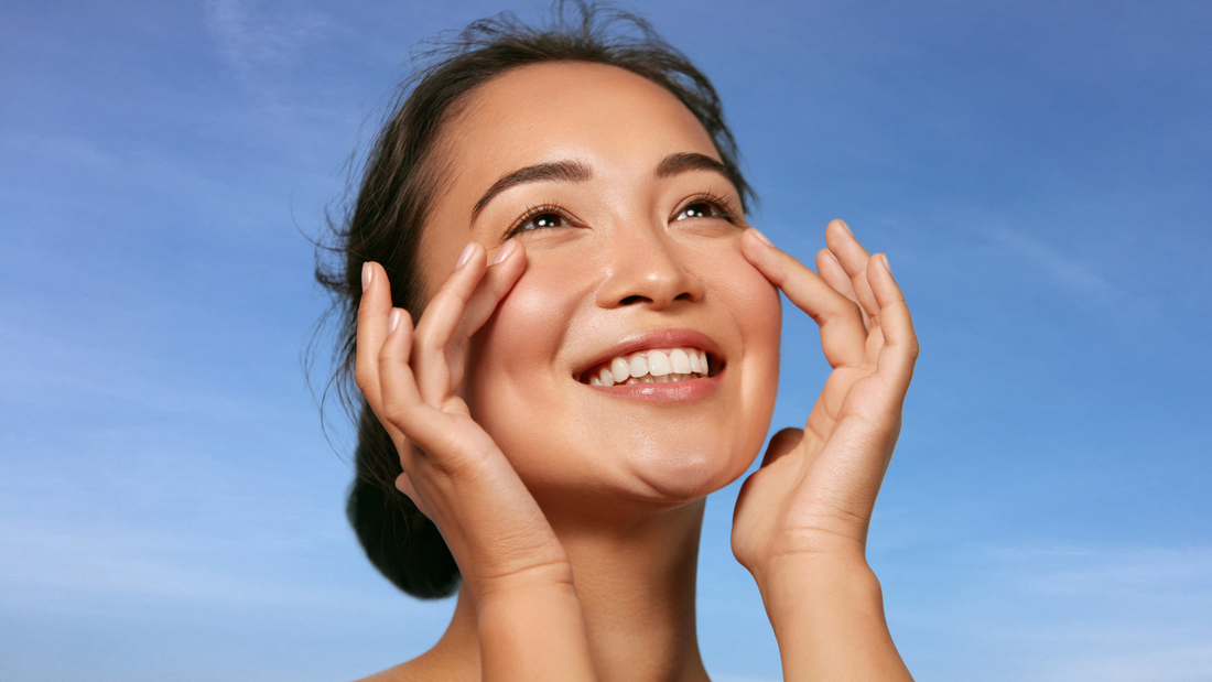 Picture of healthy Asian woman smiling in front a clear, blue sky and showing off her glowing complexion, demonstrating the benefits of collagen for women and skin.